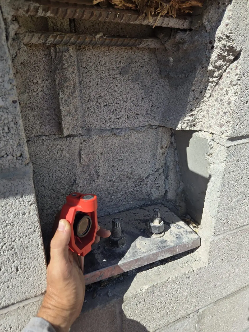 Mini survey prism held over anchor bolts on a steel base plate in a block wall