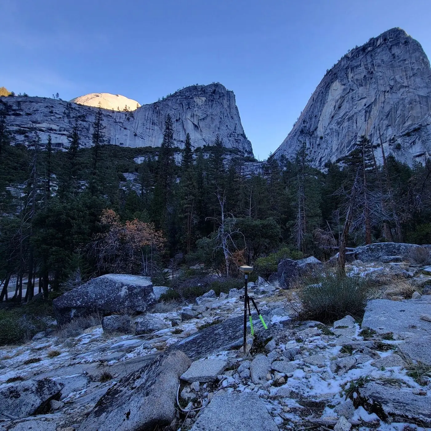 Granite domes above a forested valley in Yosemite with survey equipment on rock in the foreground