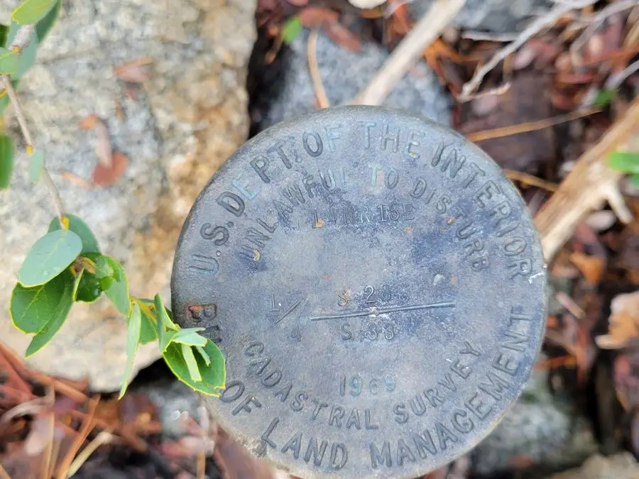 Weathered Bureau of Land Management cadastral survey cap among leaves and rocks