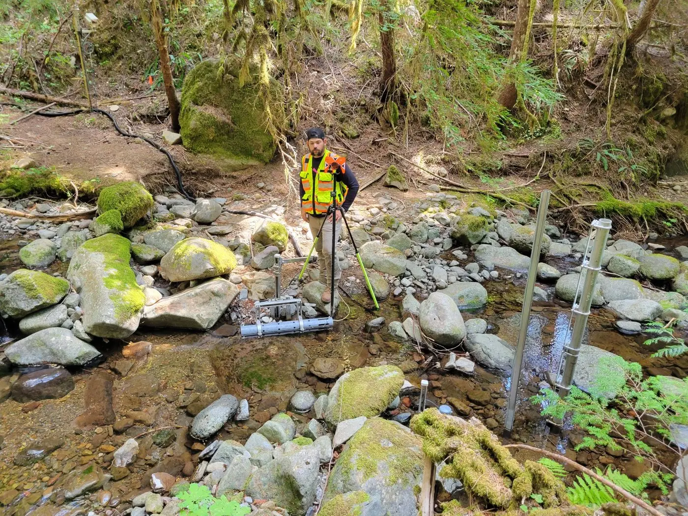 Surveyor with a prism on a tripod in a mossy forest stream among research instruments